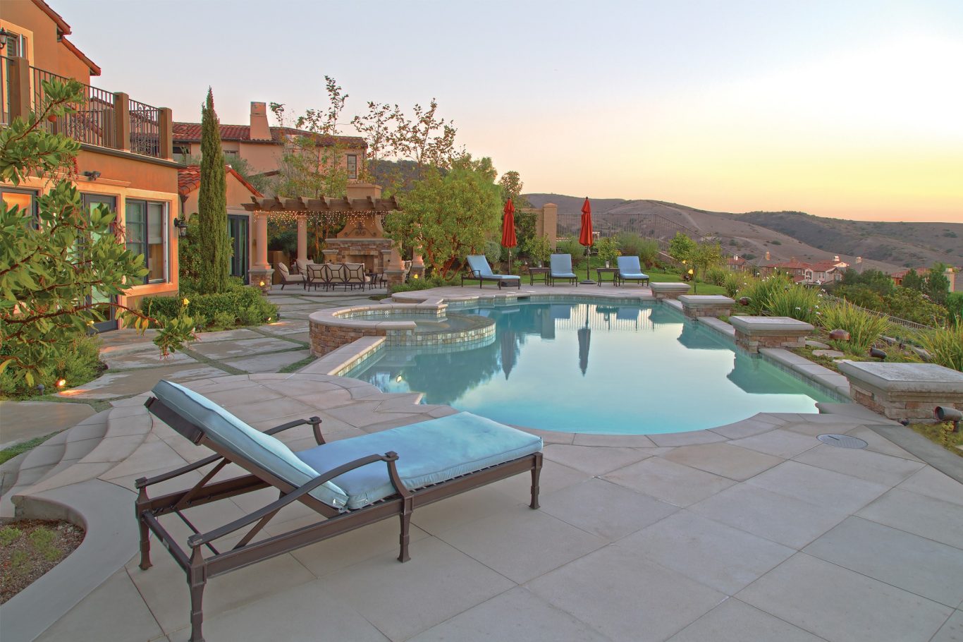 Erdspießlautsprecher Elegante Terrasse mit Pool und Liegen, umgeben von sanften Hügeln bei Sonnenuntergang.