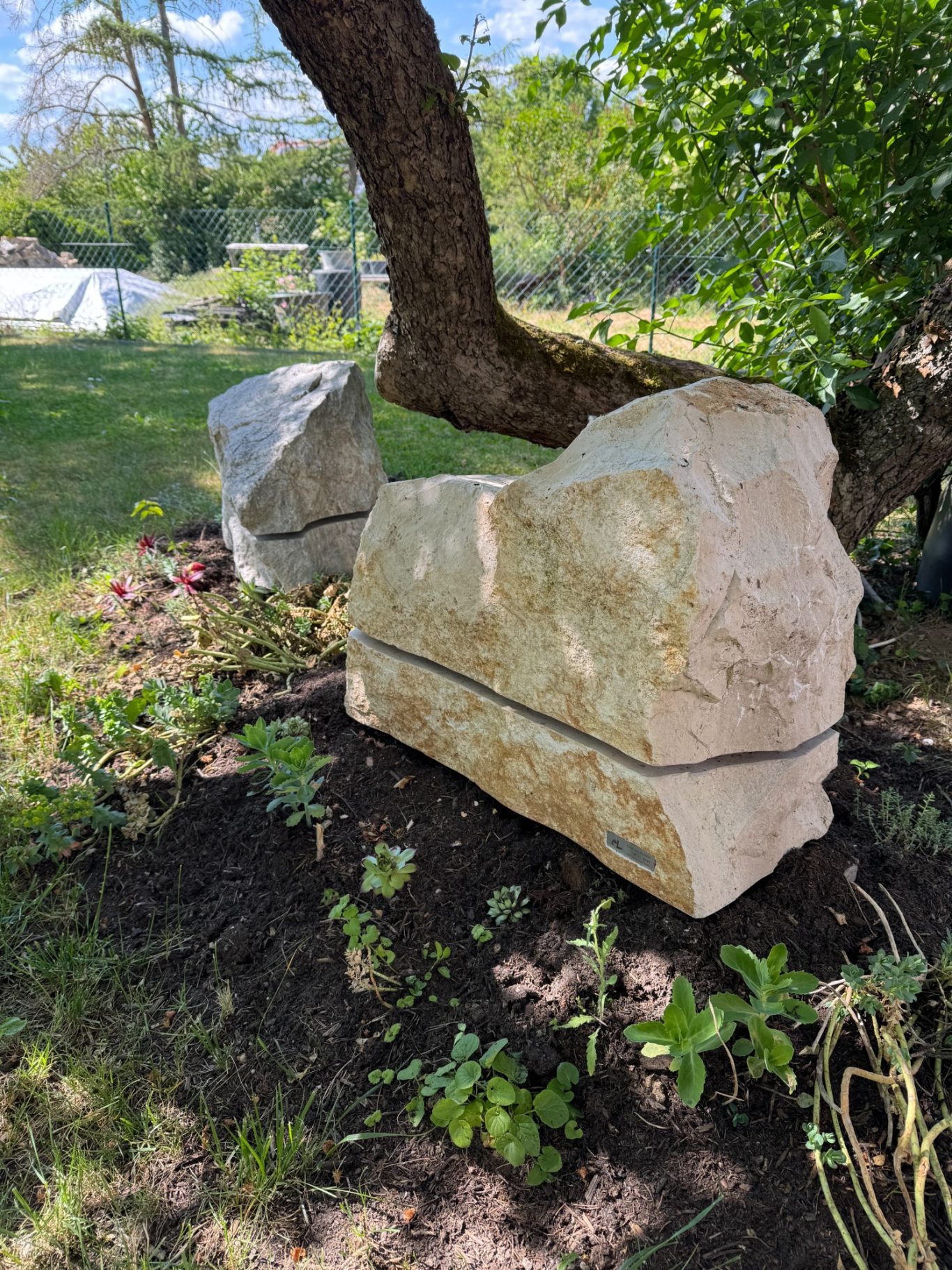 Steinlautsprecher Zwei große Steine im Garten, umgeben von Pflanzen und Bäumen.