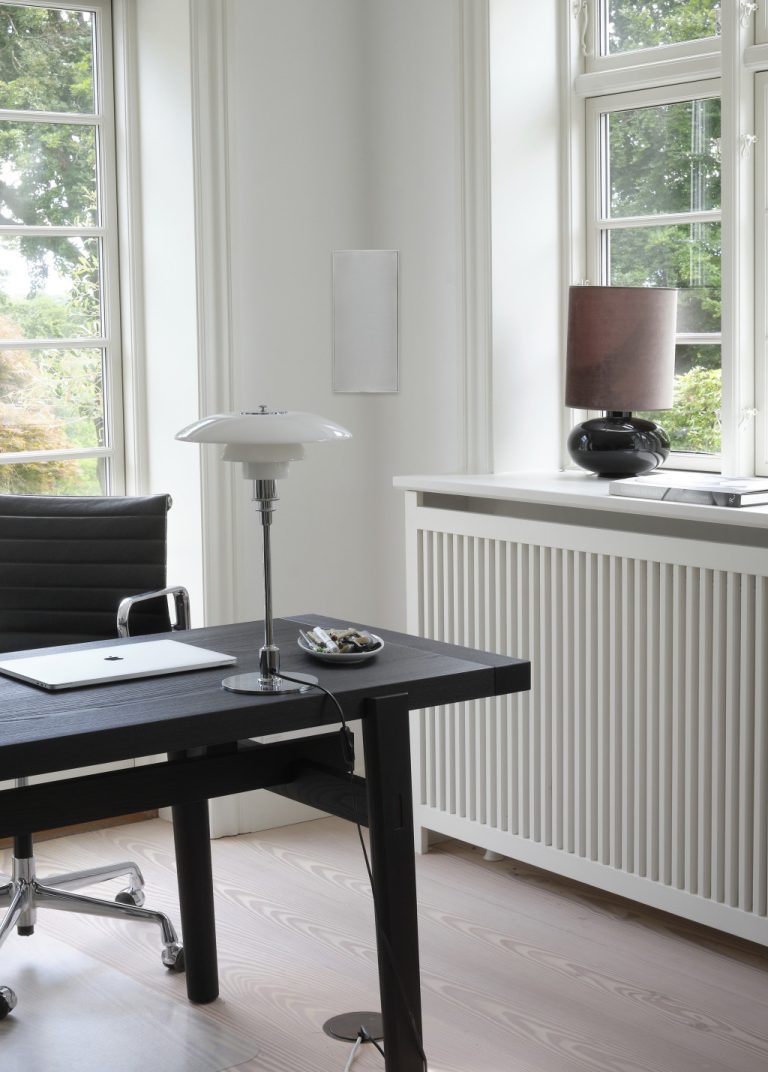 Ecklautsprecher Schreibtisch mit Stuhl, Lampe und Fensterblick auf eine grüne Umgebung.