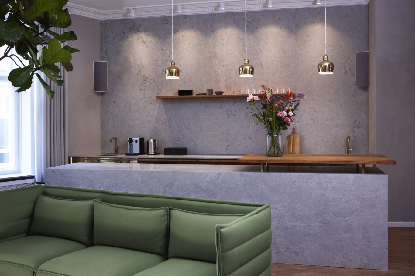 Ecklautsprecher Moderne Wohnküche mit grüner Sofa-Ecke, Holzregal und blühendem Blumenarrangement.