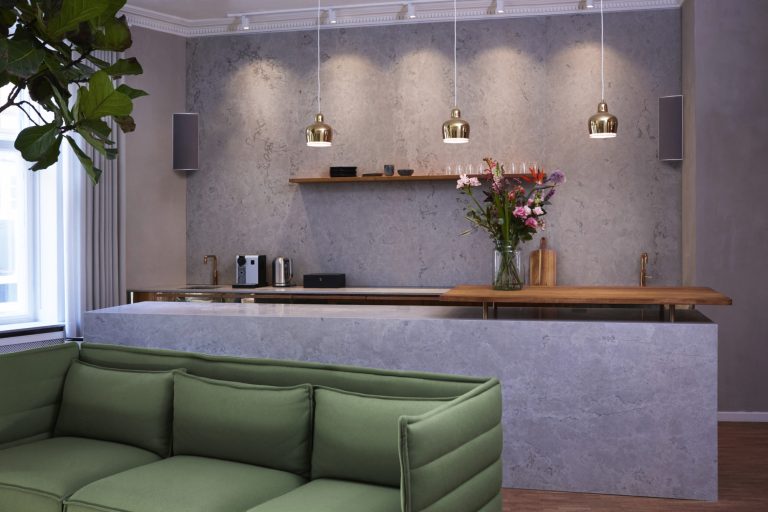 Ecklautsprecher Moderne Wohnküche mit grauen Wänden, grüner Couch und hängenden Lampen.