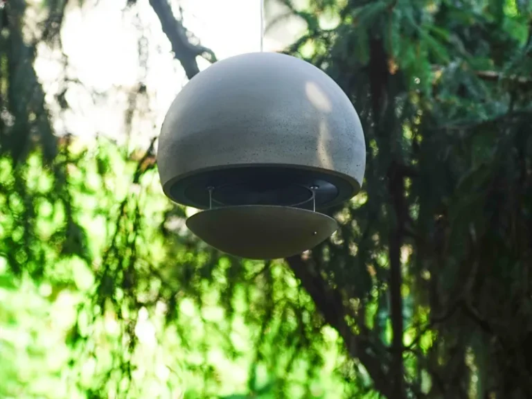 Pendellautsprecher Runde, schwebender Lautsprecher zwischen grünem Laub im Hintergrund.