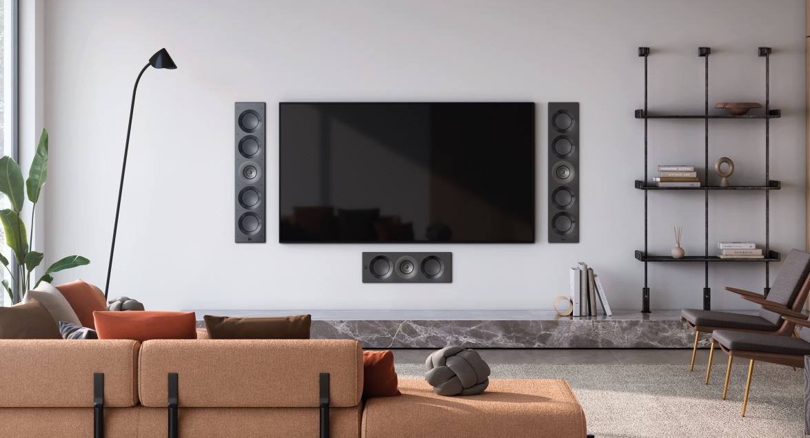 Wandeinbaulautsprecher Wohnzimmer mit einem großen Fernseher, Sofa, Bücherregal und einer Stehlampe.