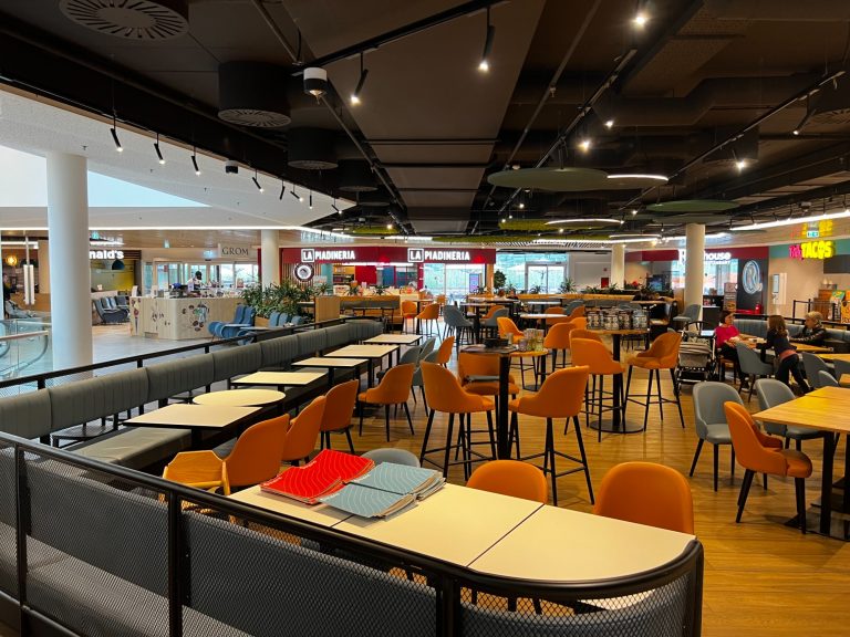 Stromschienenlautsprecher Moderne Essenshalle mit vielen Tischen, Stühlen und einer einladenden Atmosphäre.