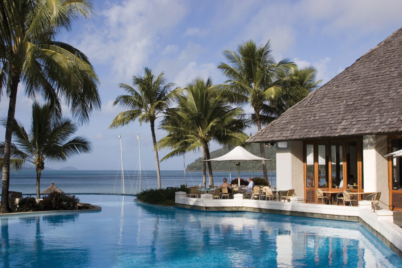 Außenlautsprecher Tropisches Resort mit Pool, Palmen und Meerblick unter blauem Himmel.