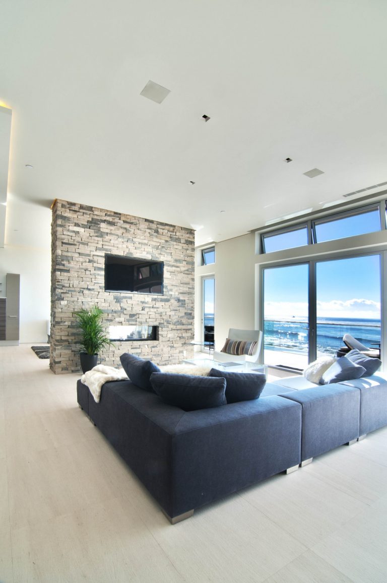 Deckenlautsprecher Moderner Wohnraum mit Steinkamin, großen Fenstern und bequemen Möbeln.