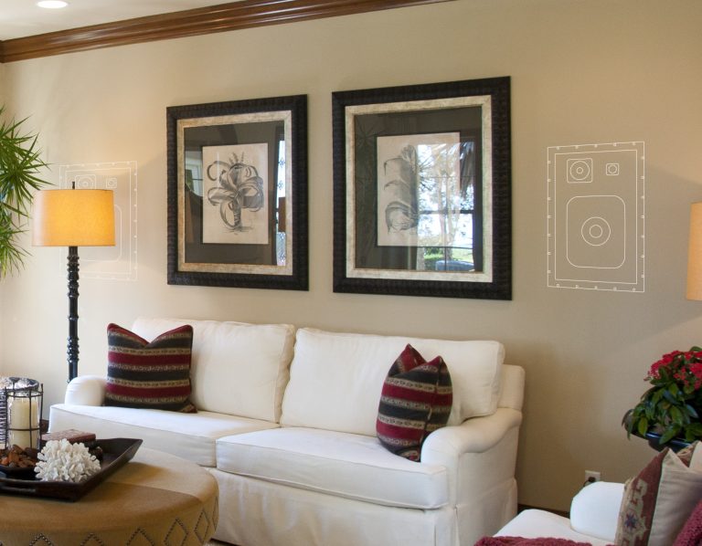 Unsichtbare Lautsprecher Helles Wohnzimmer mit weißem Sofa, zwei Bildern an der Wand und dekorativen Pflanzen.